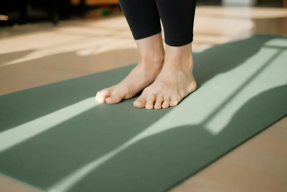 Bare feet standing on a green exercise mat in morning light